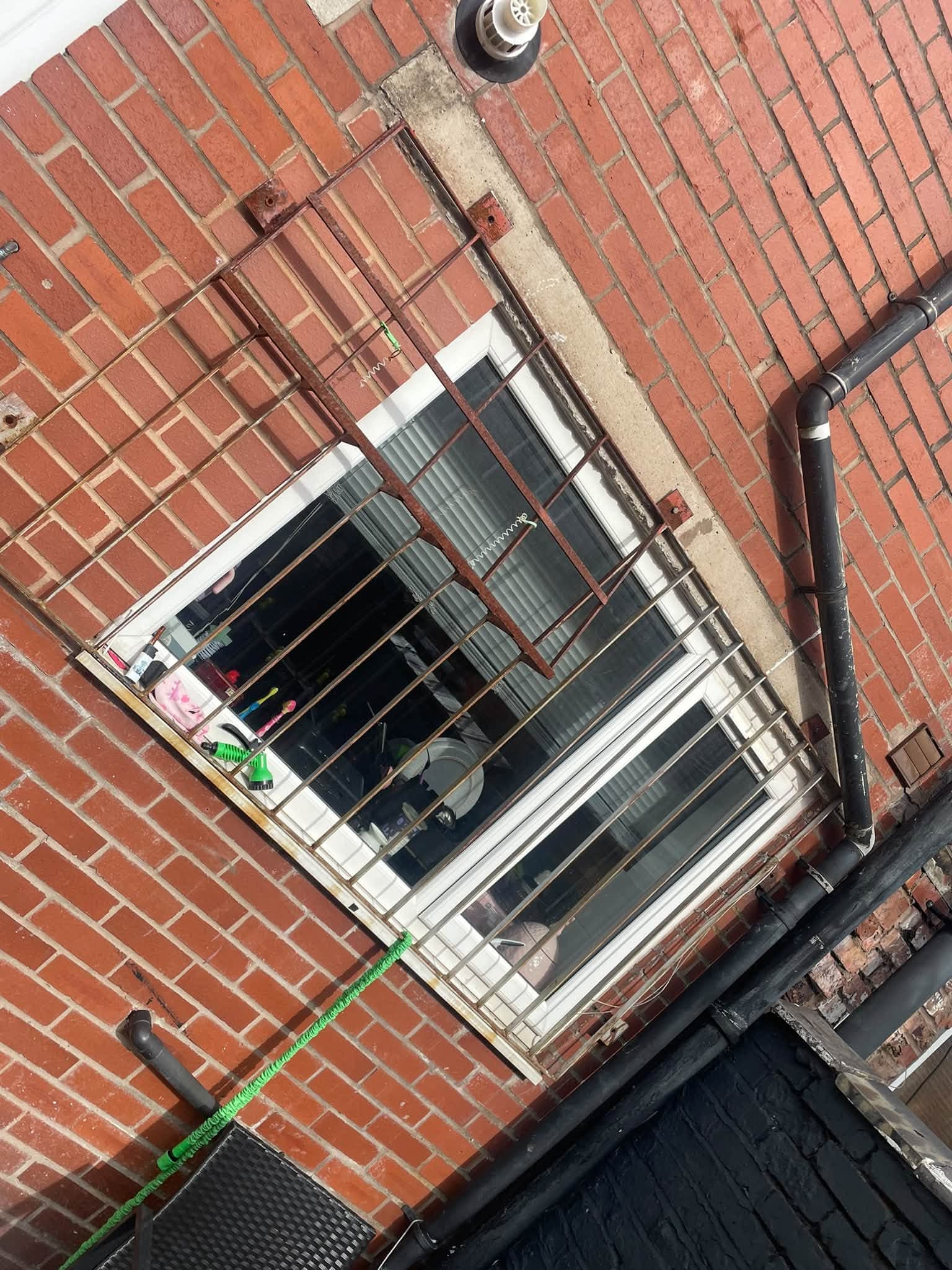 Metal window security bars being fitted to an exterior brick wall